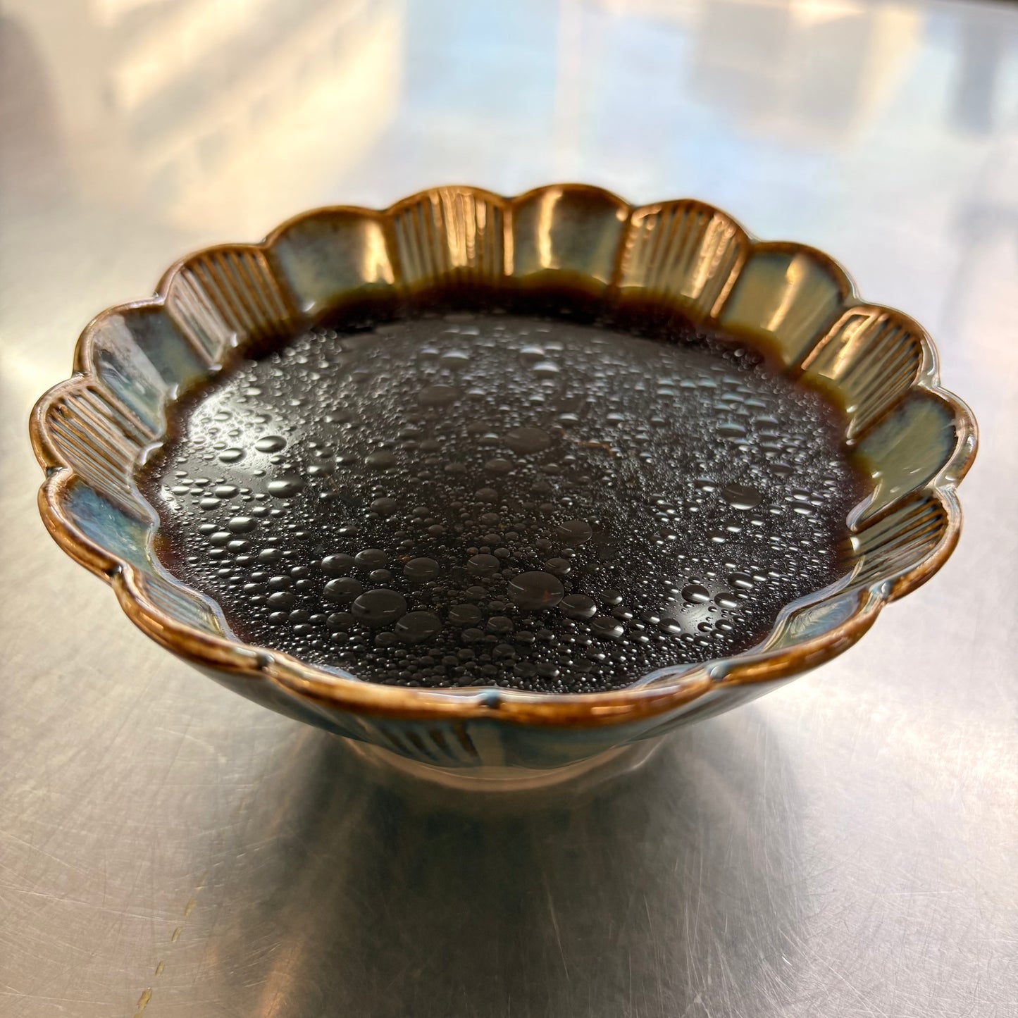 Bowl of savory sauce for herbal braised chicken leg with a glossy finish and condensation