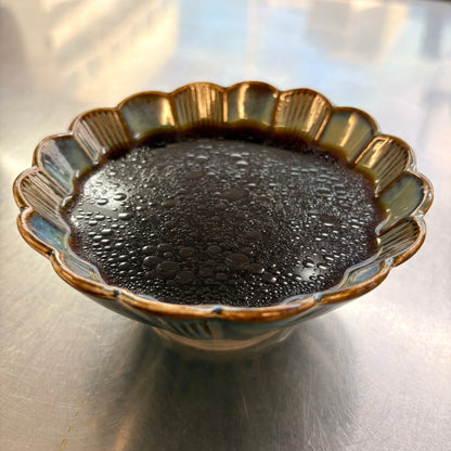 Bowl of savory sauce for herbal braised chicken leg with a glossy finish and condensation